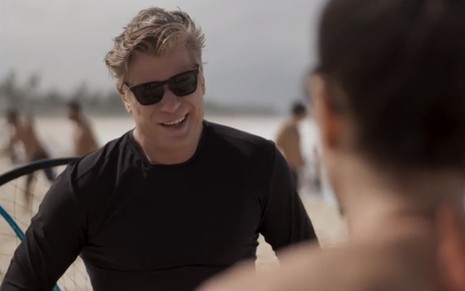 O ator Fabio Assunção de óculos escuro, sorrindo, em cena como Arthur na novela Totalmente Demais