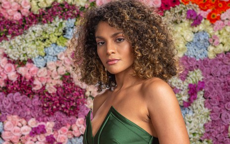 Barbara Reis usa um vestido verde e posa com o fundo de flores