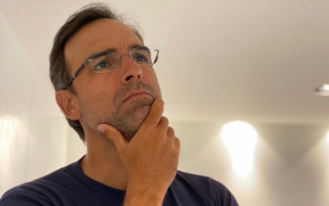 Imagem de Tadeu Schmidt de camiseta preta e óculos, com a mão no queixo
