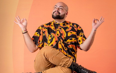 Tiago Abravanel está sentada com uma blusa preta com detalhes em laranja e amarelo na posição zen