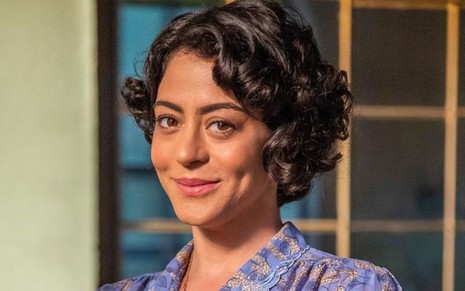 Carol Castro sorri discretamente e usa roupas de época em caracterização da novela Amor Perfeito