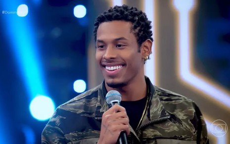 Paulo André com um uma camisa preta e sorrindo no palco do Domingão, logo após chorar