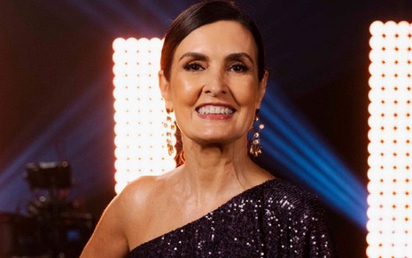 Fátima Bernades com um sorriso, usando uma blusa preta em uma chamada da Globo