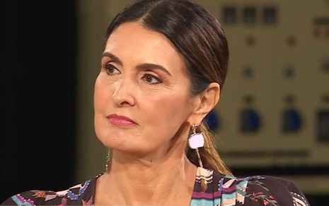 Fátima Bernardes com um brinco branco, rabo de cavalo e olhando para o horizonte com uma cara de desconfiada com alguma coisa