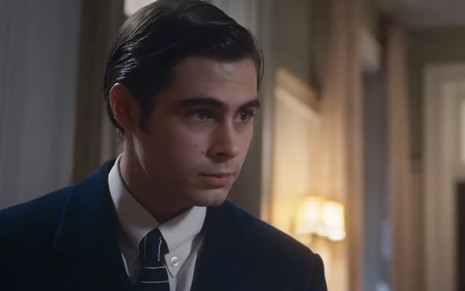 O ator Rafael Vitti em cena como Davi na novela Além da Ilusão; ele está com uma expressão tensa e usa terno e gravata