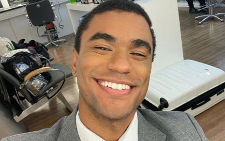Isacque Lopes caracterizado como Ben; ele usa um terno cinza e sorri para a câmera nos bastidores de Vai na Fé