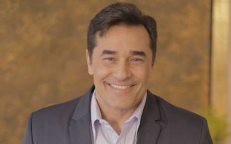 Luciano Szafir está vestido com terno e sorri para foto