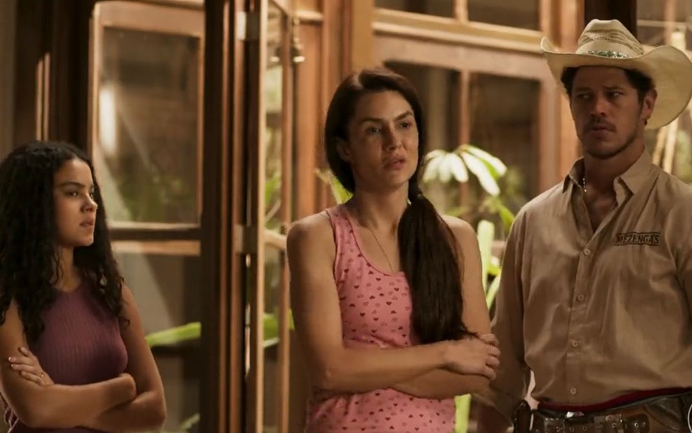 A atriz Paula Barbosa como Zefa em Pantanal, entre a atriz Bella Campos como Muda e o ator José Loreto como Tadeu; ela está com os braços cruzados e cara de desanimada entre os dois que olham atentamente para ela