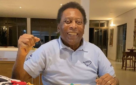 Pelé sorri, está vestindo uma camiseta azul e está com um braço levantado