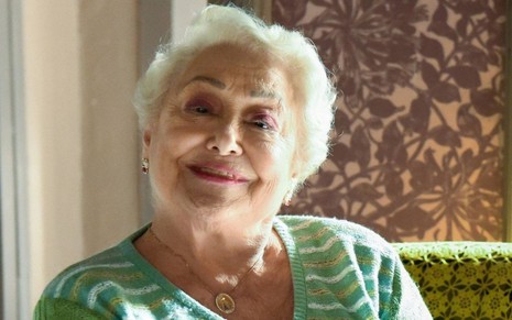 Com os cabelos bem brancos, Suely Franco posa sorrindo para foto; ela veste uma blusa verde pastel com listas brancas e usa uma maquiagem leve