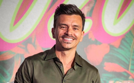 Gustavo Reiz sorrindo em frente a painel colorido, na festa de lançamento de Fuzuê