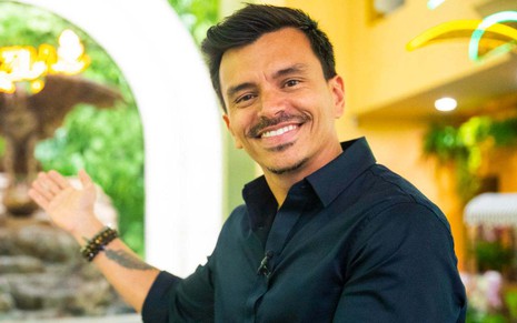 Gustavo Reiz sorri e aponta para cenário da novela Fuzuê