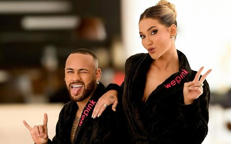 Neymar e Virginia Fonseca posam juntos, ambos vestem roupão preto, e ela coloca a mão no ombro do jogador