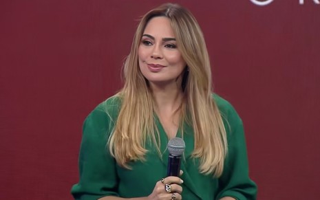 Rachel Sheherazade no evento de lançamento da nova temporada de A Grande Conquista, com expressão séria, segurando microfone