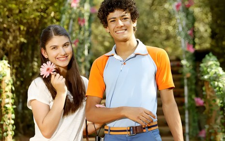 Giovanna Grigio e Gabriel Santana estão sorridentes nos bastidores de Chiquititas; ela segura uma flor