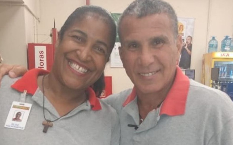 A fã Rosemeri Albino posando em foto com o ator Eri Johnson em supermercado; os dois usam uniformes do estabelecimento